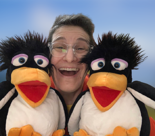 Sara - woman smiling with short dark hair and glasses with two penguin puppets