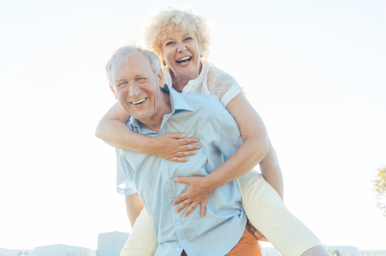 Grey haired man giving grey haired woman a piggy back