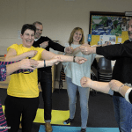 4 women and 2 men with arms stretched to one side laughing