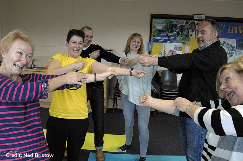 4 women and 2 men with arms stretched to one side laughing
