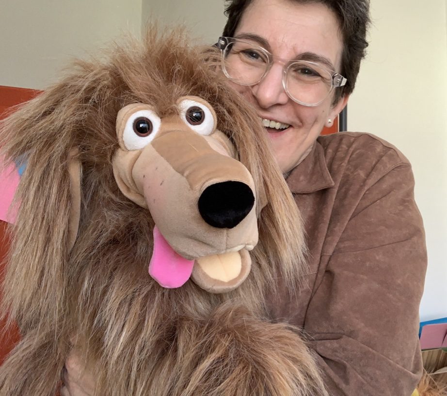 Dog puppet with Sara Kay woman short brown hair and glasses wearing a brown coat