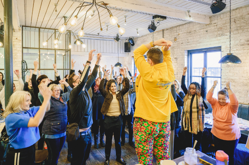 Corporate networking Laughter Yoga event with one man and 22 women laughing with arms in the air